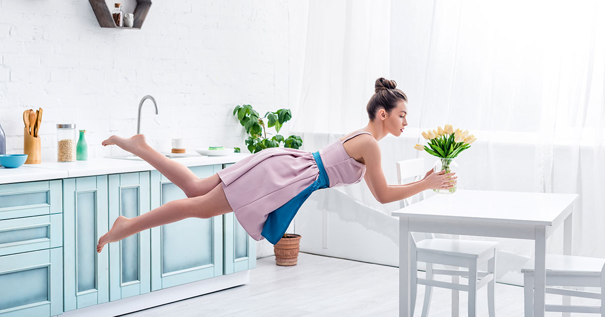 Junge elegante Frau schwebt barfuß mit Tulpen in der Luft in einem Haus
